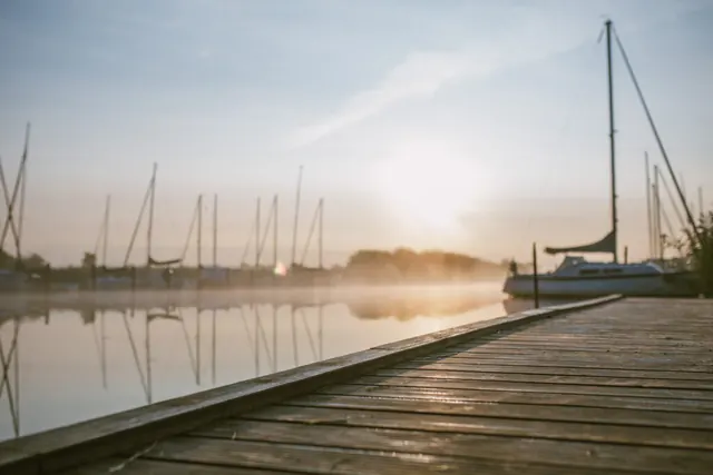 Steg und Segelboote am Ryck in Greifswald bei Sonnenaufgang, Nebel über dem Wasser.